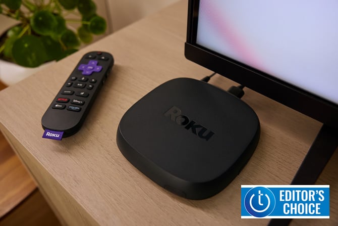 Roku Ultra 2024 with remote control on wooden table with TV. The Techlicious Editor's Choice Award logo is in the lower right corner.