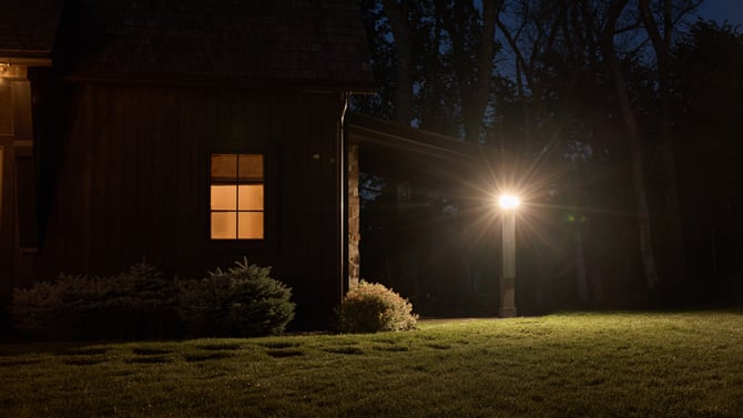 Arlo Wired Floodlight Camera is mounted on a post in a yard at night.