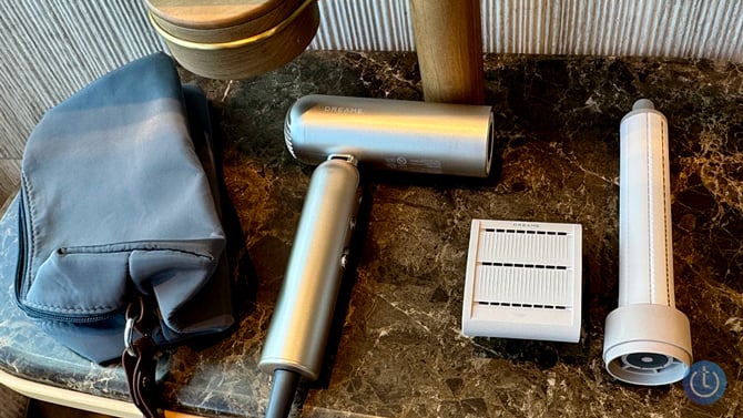 The Dreame Pocket hair dryer is shown with its bag and the unfrizz attachment (lto the right of the dyer) and curling attachment (to the right of the unfrizz attachment)).