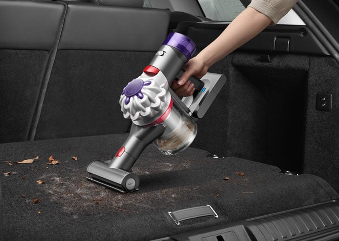 The Dyson Car+Boat handheld vac is shown cleaning the back of a car.