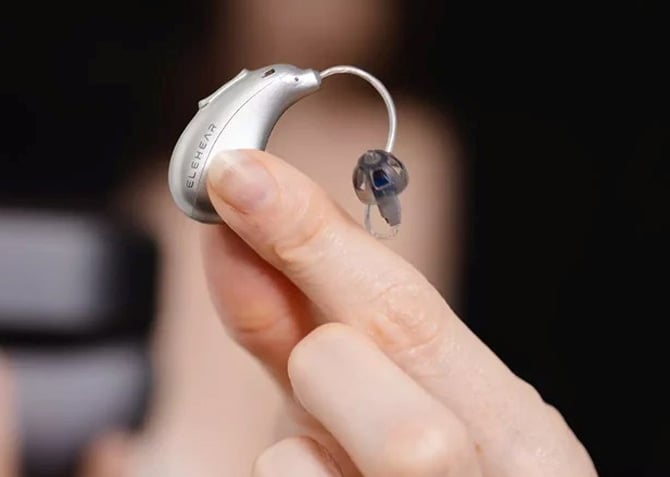 Elehear Beyond small profile over hte ear bud held between finger tips