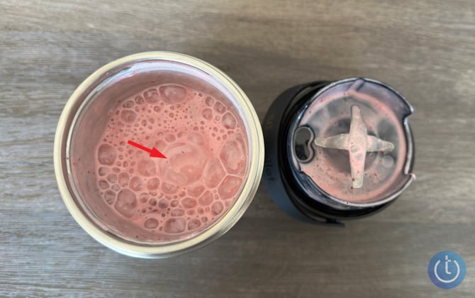 Nutribullet Flip insulated cup with a smoothie inside and the blending top with the blades showing. An ice cube is pointed out.