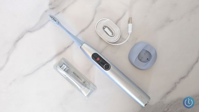 Oclean X Pro is shown with an additional brush head, the charging cable, and wall mount.