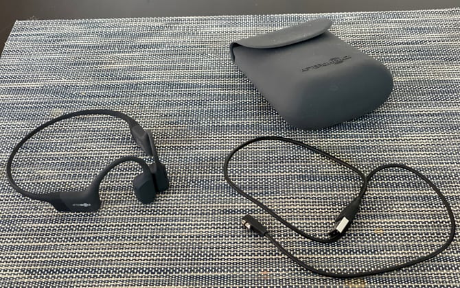 AfterShokz Aeropex headphones on mat with case and charging cable. 