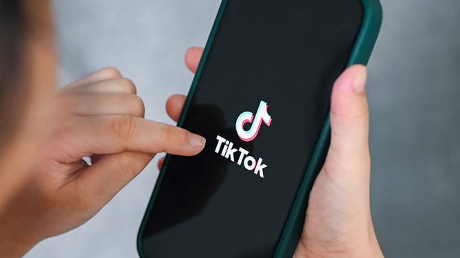 A child holds a phone showing the TikTok logo.