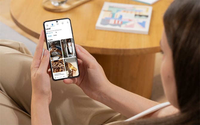 Woman holds a phone showing a screenshot of the Local feed for Facebook