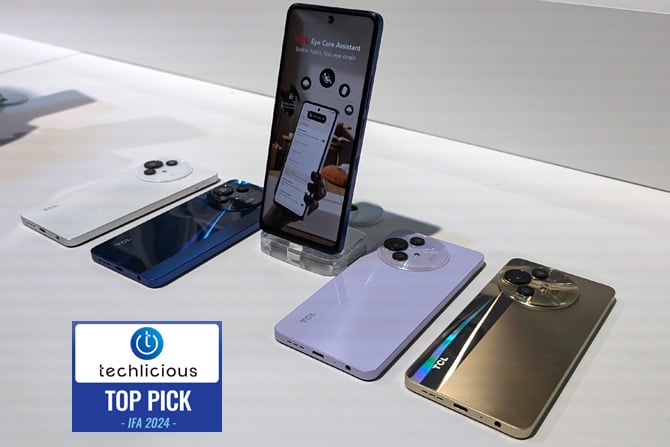  The TCL 50 Pro NXTPaper 5G phone is shown on a stand with several more showing available colors: from the left are white, blue, purple, and gold.  The Techlicious Top Pick Award logo is in the lower left.